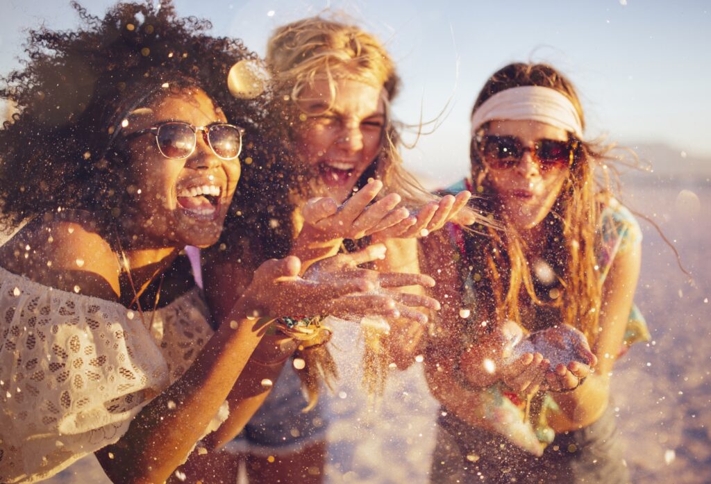 tre ragazze su una spiaggia si divertono soffiando la sabbia